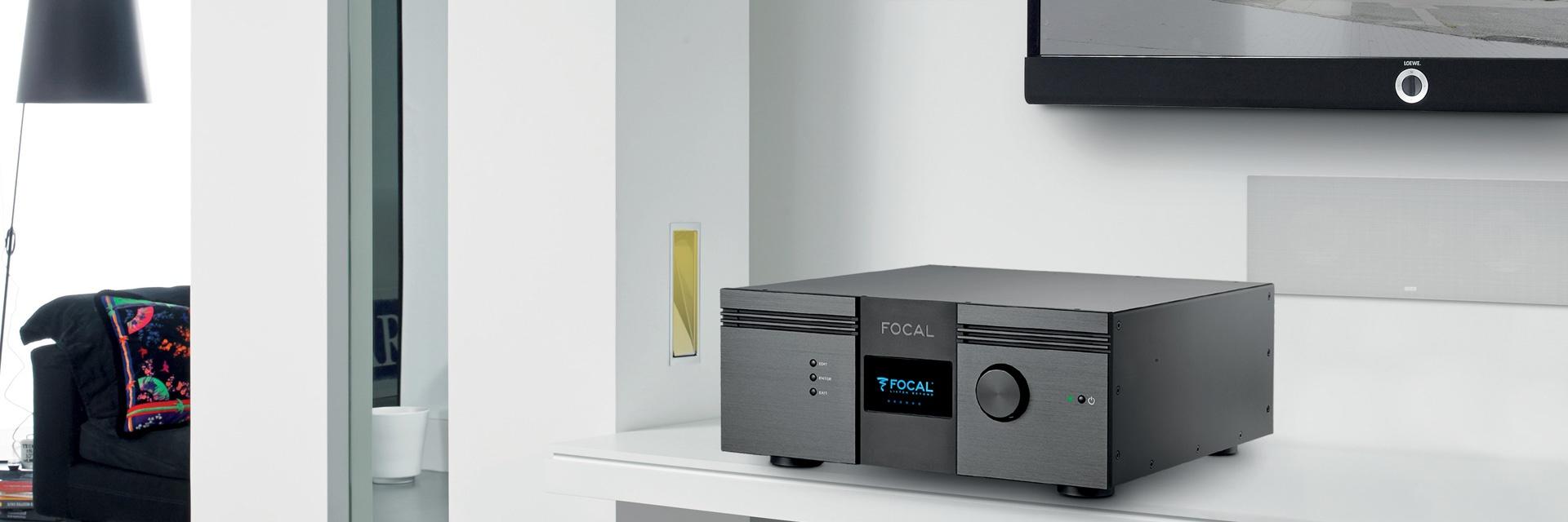 Close-up of black Focal amplifier placed on white shelf beneath a TV